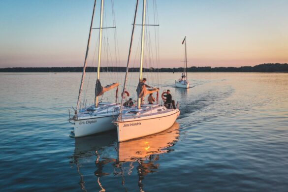 dwa jachty płyną holując się burta przy burcie przy zachodzącym słońcy